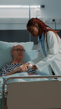 Hastane koğuşundaki hastanın eline oksimetre takan doktor.