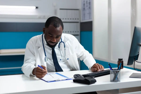 Médico afro-americano datilografa tratamento de saúde no computador — Fotografia de Stock