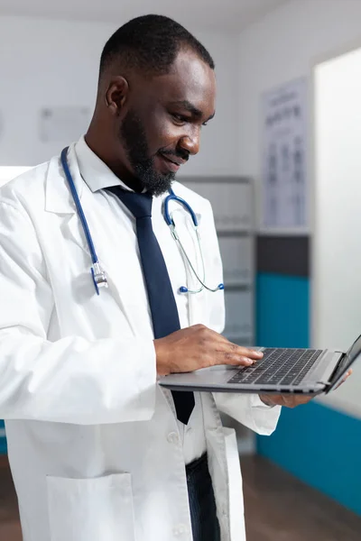 Médico afro-americano com estetoscópio digitando experiência médica no laptop — Fotografia de Stock