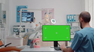 Yatay yeşil ekranlı monitör kullanan diş asistanı