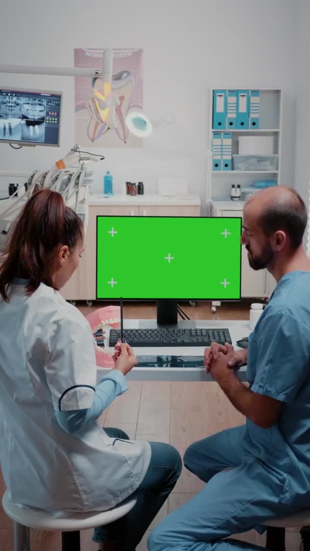 Dikey video: Bilgisayarda yeşil ekrana bakan dişçi ve asistan — Stok video