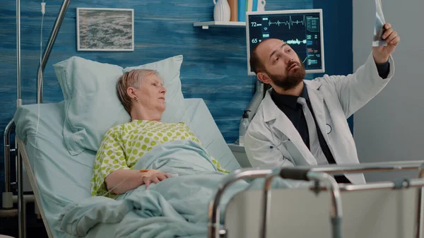 Dokter en oudere vrouw in bed op zoek naar x ray scan — Stockfoto