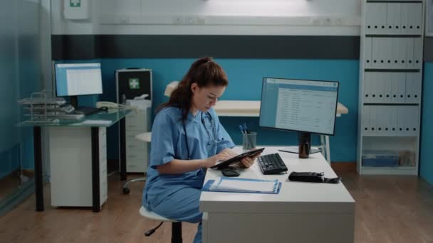 Asistente médico escribiendo en la pantalla de la tableta y comprobando el ordenador — Vídeo de stock