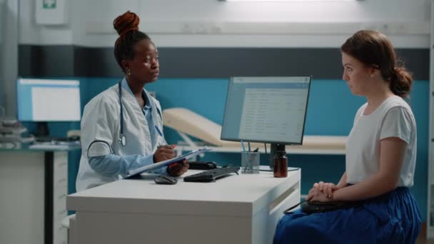 Az orvos jegyzetel a vizsgálati papírokról és beszél a beteg beteggel. — Stock videók