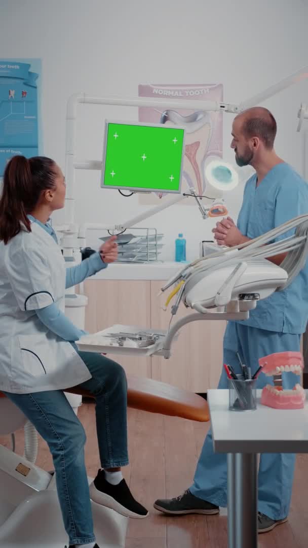 Vertikales Video: Zahnarzt und Assistent arbeiten mit grünem Bildschirm — Stockvideo