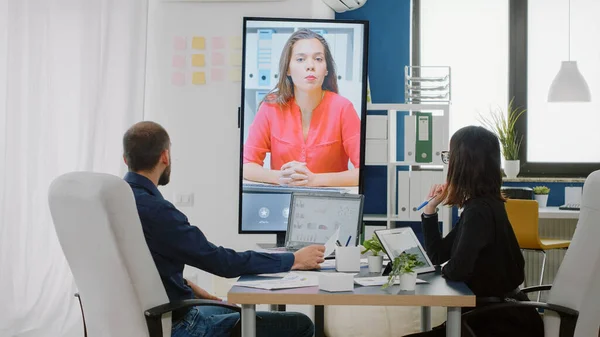 Compañeros de trabajo usando videollamada en televisión para conversar con una mujer —  Fotos de Stock