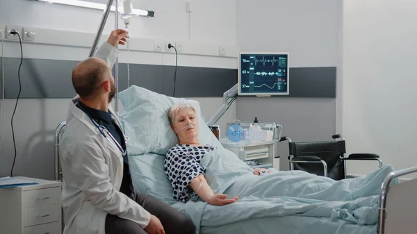 Arts en verpleegkundige controleren op oudere patiënt in ziekenhuisafdeling bed — Stockfoto