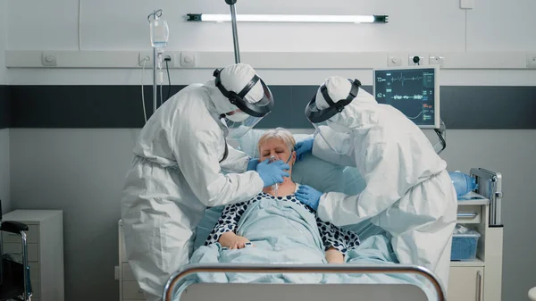 Squadra medica con tute e maschere per aiutare il paziente a respirare pesantemente — Foto Stock