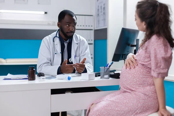 Mulher com gravidez discutindo com especialista sobre cuidados médicos — Fotografia de Stock