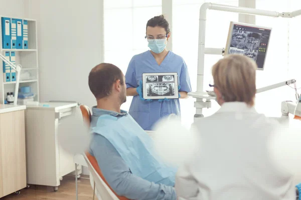 Медсестра-ортодонт держит на экране цифровой планшет с рентгенографией зубов — стоковое фото