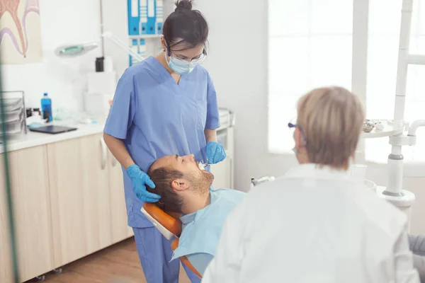 Медицинская сестра делает профессиональную чистку зубов человеку пациенту — стоковое фото