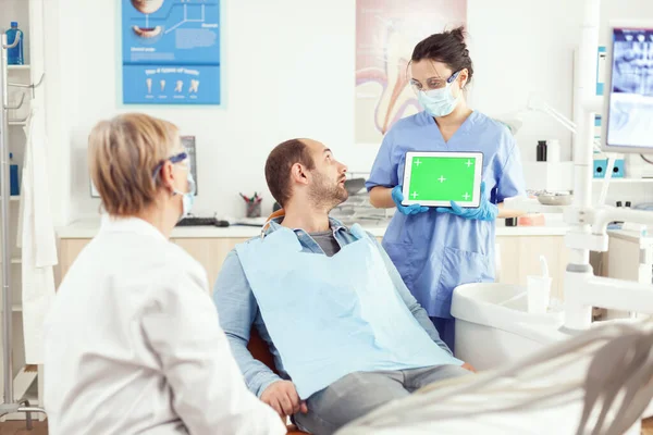 Хворий пацієнт дивиться на сенсорний гаджет, розмовляючи зі стоматологом старшим лікарем — стокове фото