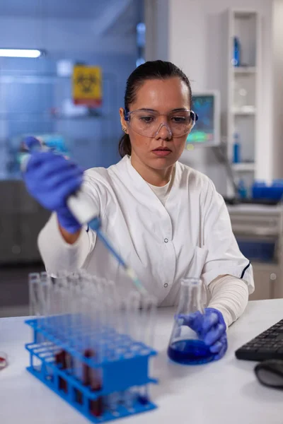 Científica mujer sosteniendo micropipeta soltando solución azul —  Fotos de Stock