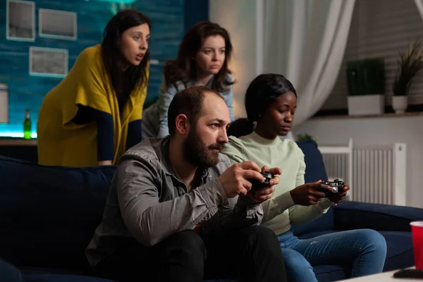 Серйозні концентровані багатоетнічні друзі сидять на дивані, тримаючи джойстик — стокове фото