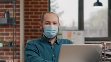 Yüz maskesi takan ve laptop kullanan bir iş adamı portresi.