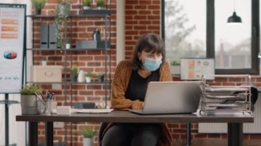 Yüz maskeli neşeli kadın laptoptan iyi haberler okuyor.