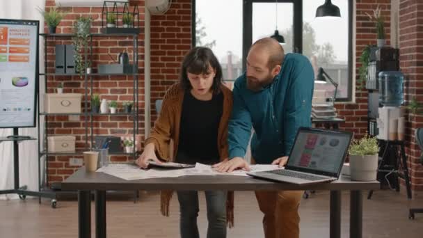 Zakenmensen controleren laptop en tarief grafieken papieren — Stockvideo