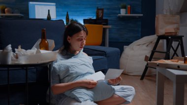 Çaresiz genç kadın gözyaşları içinde yerde oturmuş kitap okuyor.