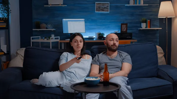 Couple spending evening dressed in pajamas arguing for remote control