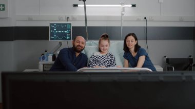 Hastane koğuşunda televizyonda çizgi film izleyen aile.
