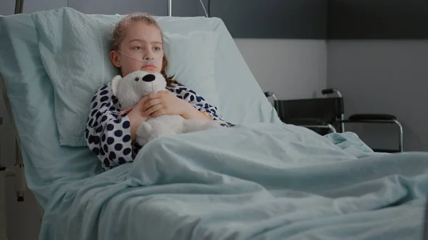 Paciente niño preocupado solo usando tubo nasal de oxígeno descansando en la cama sosteniendo oso teedy —  Fotos de Stock
