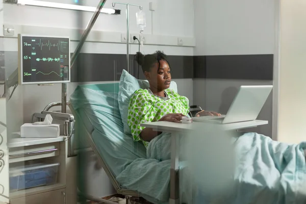 Africano paciente doente americano em pé na cama durante o exame médico assistindo filme engraçado online — Fotografia de Stock