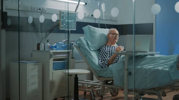 Oudere zieke patiënt met laptop in ziekenhuisbed — Stockfoto