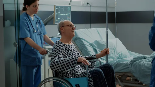 Oudere patiënt verlaat ziekenhuisafdeling in rolstoel — Stockfoto