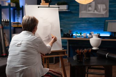 Yaşlı kadın tuvalden vazo tasarımı çiziyor.