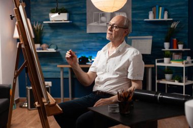 Tuval üzerine çizim yapmak için elinde kalem tutan yaşlı bir sanatçı.