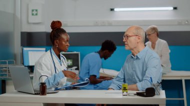 Sağlık uzmanı masadaki eski bir hastayla konuşuyor.