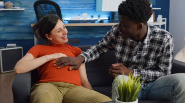 Evdeki koltukta oturan ırklar arası hamile bir çift.