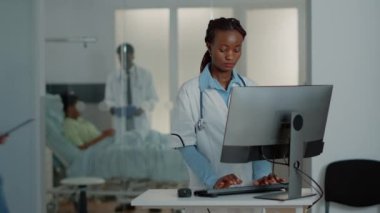 Masasında bilgisayar kullanan beyaz önlüklü pratisyen.