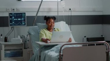 Genç hasta yatağındaki modern laptopta video kullanıyor.