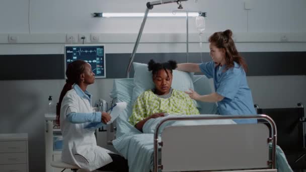 Африканський американець і жінка, які консультують пацієнта в ліжку. — стокове відео