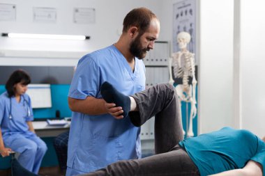 Kayropraktik doktoru yaşlı kadına bacak kası ağrısı için yardım ediyor.