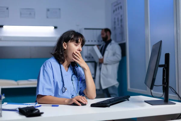 Uitgeputte verpleegster met behulp van de computer op het bureau terwijl ze in slaap valt — Stockfoto