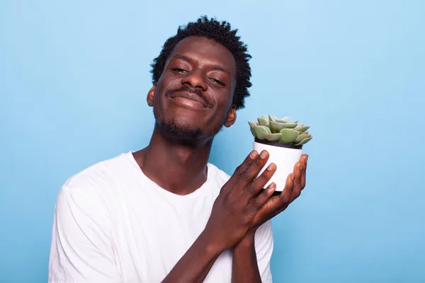 Uomo allegro che tiene piccolo vaso con pianta e sorridente — Foto Stock