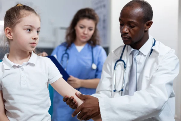 Médico pediatra afroamericano frotando brazo fracturado de niña —  Fotos de Stock