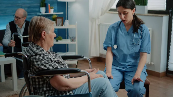 Літня жінка з обмеженими можливостями в будинку престарілих розмовляє з медсестрою — стокове фото