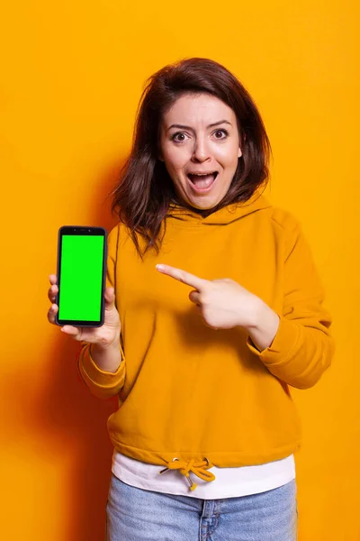 Mujer joven apuntando a la pantalla verde vertical en el teléfono inteligente — Foto de Stock