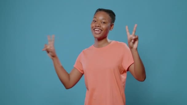 Vidám nő csinál béke szimbólum ujjaival és mosolygós — Stock videók