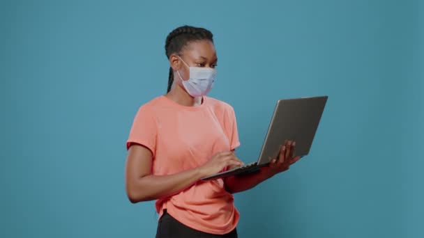 Junger Erwachsener mit Gesichtsmaske hält modernen Laptop im Studio — Stockvideo