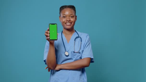 Uśmiechnięta pielęgniarka pokazuje zielony ekran na telefonie komórkowym przed kamerą — Wideo stockowe