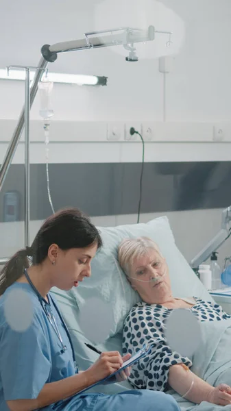 Medische assistent doet checkup bezoek voor patiënt in ziekenhuisafdeling bed — Stockfoto