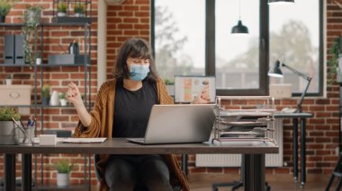 Yüz maskeli neşeli kadın laptoptan iyi haberler okuyor.