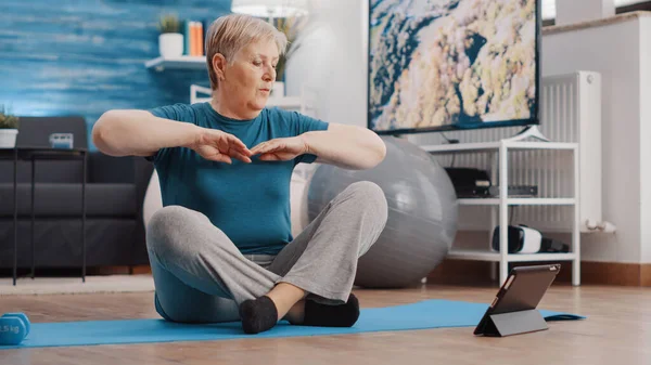 Aged person doing physical exercise and watching workout video