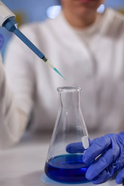 Крупный план специалиста-исследователя, сбрасывающего медицинский синий раствор в стеклянную посуду — стоковое фото