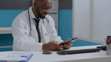 Afrika kökenli Amerikalı terapist elinde tablet olan doktor hastalık raporlarını kontrol ediyor.