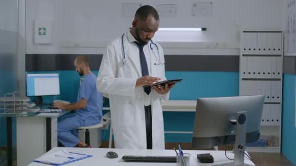 Africano terapeuta americano médico segurando tablet computador verificando relatório de sintomas da doença — Vídeo de Stock
